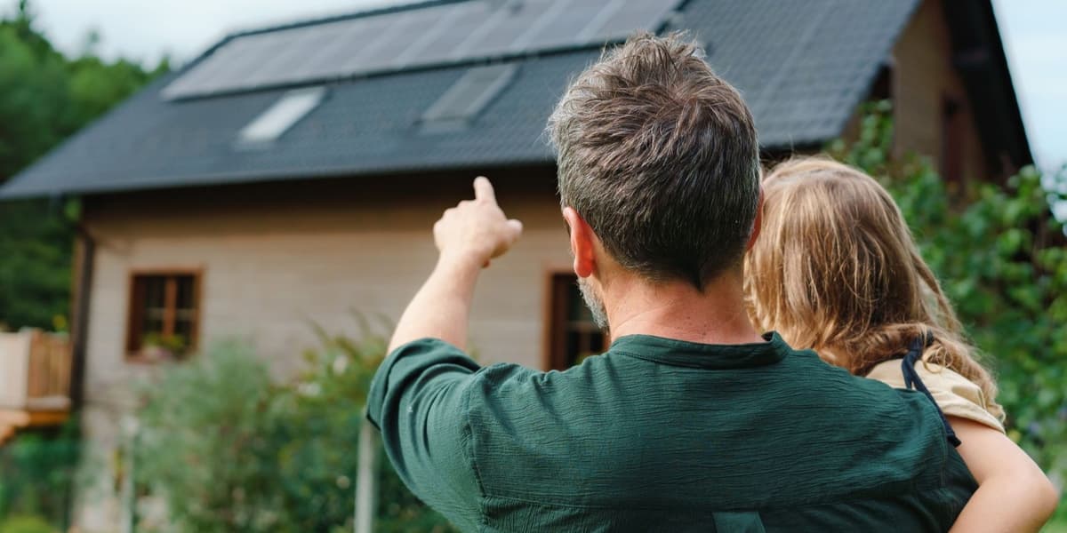 Man heeft dochter op zijn arm. Ze staan voor hun vrijstaande woning en kijken en wijzen naar het huis.