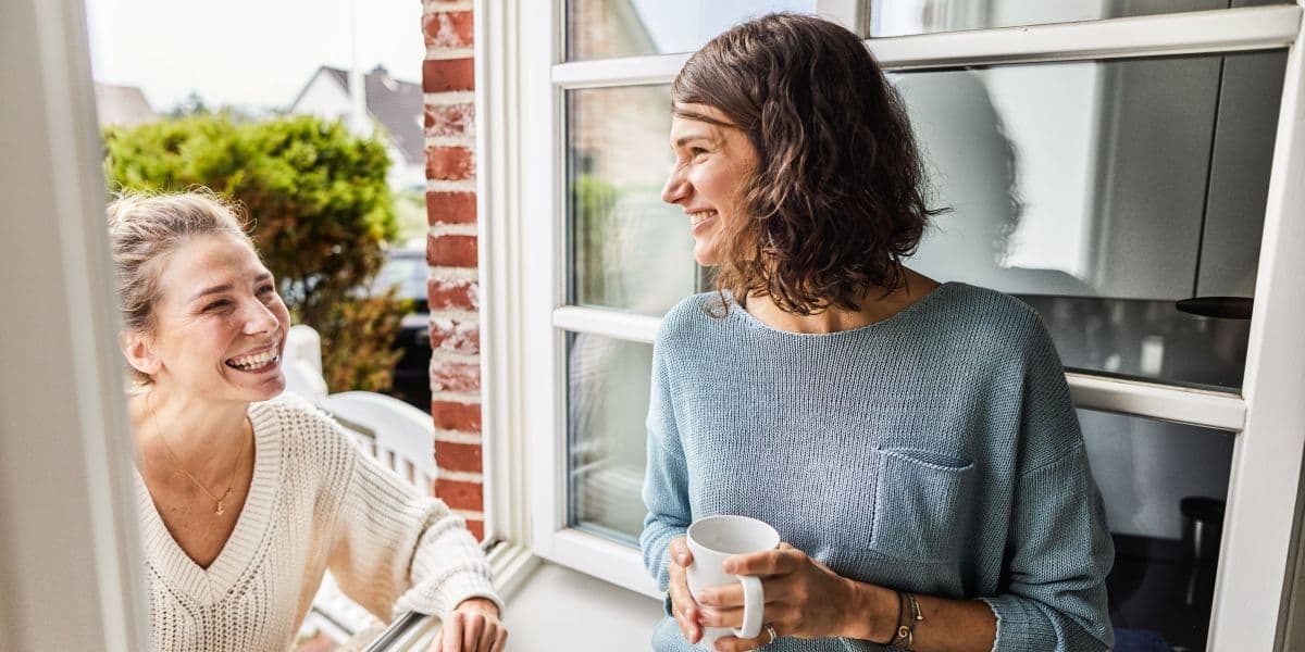 Een vrouw staat binnen in het open raam te praten met een vrouw buiten
