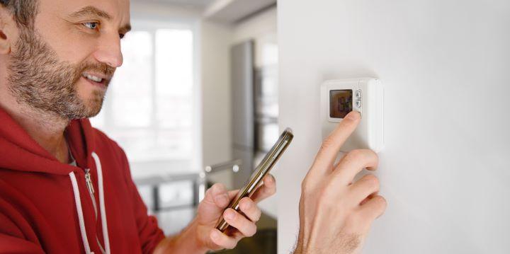 Man stelt de thermostaat van zijn huis in terwijl hij zijn telefoon in de hand houdt
