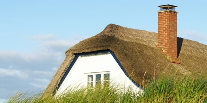 Vrijstaand huis met witte muren en een rieten dak.