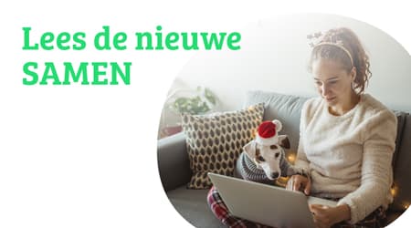 Vrouw zit met hond op schoot op de bank en leest op haar laptop het online magazine SAMEN. Links in beeld staat de tekst: ‘Lees de nieuwe SAMEN