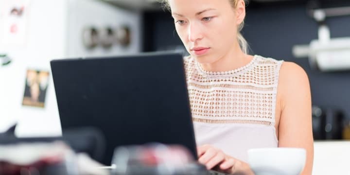 Blonde vrouw werkt op een zwarte laptop in haar woning.