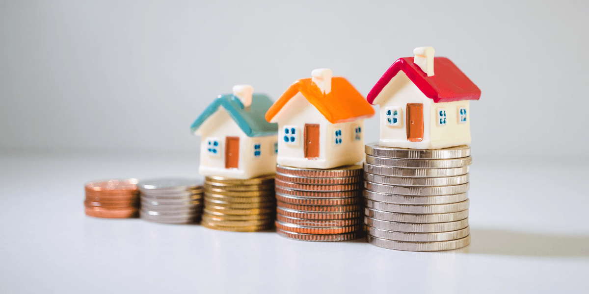 Stapeltjes met muntgeld met daarop kleine keramische huisjes.