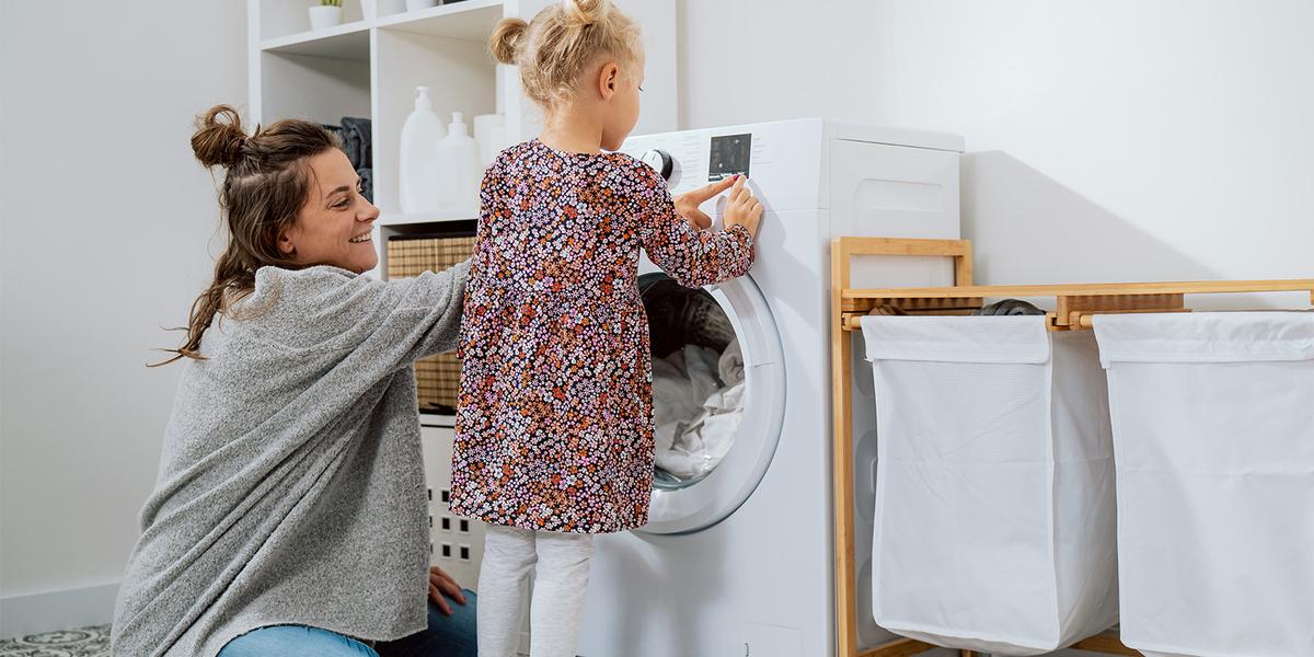 Moeder zit in de wasruimte in huis met haar dochtertje voor de wasmachine en stelt het programma in voor de witte was