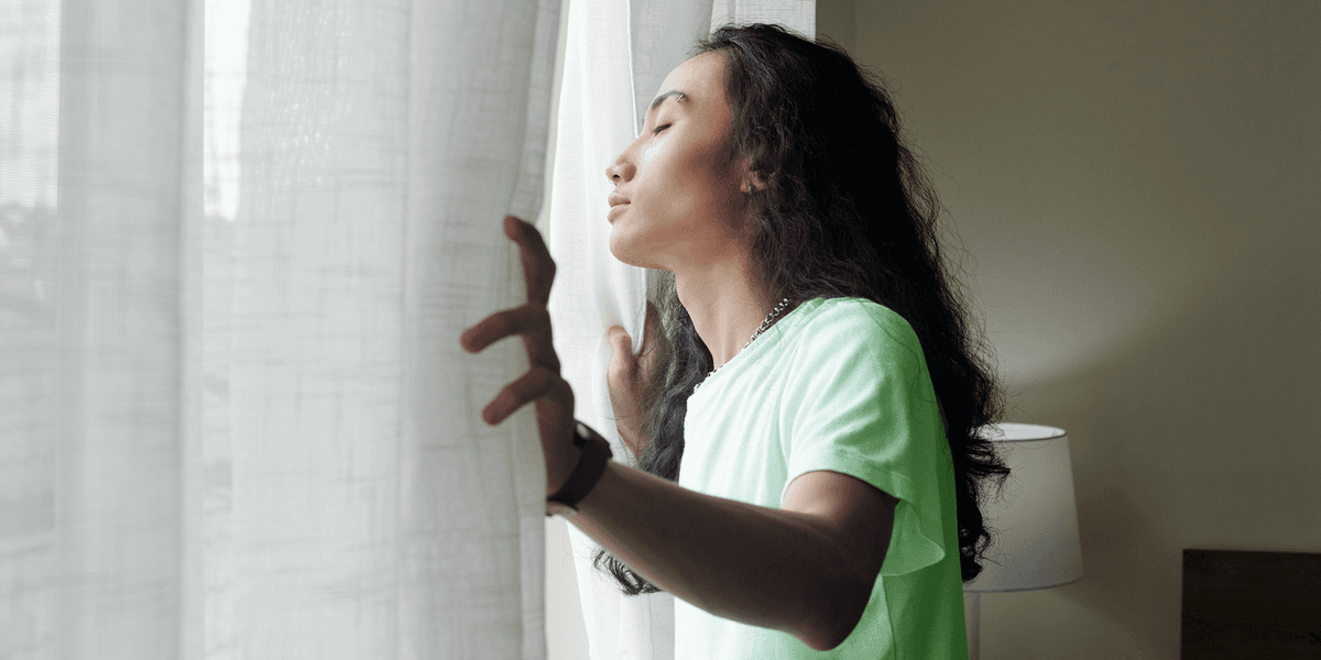 Vrouw doet de gordijnen open in de woonkamer en ademt diept in terwijl ze haar ogen dicht heeft