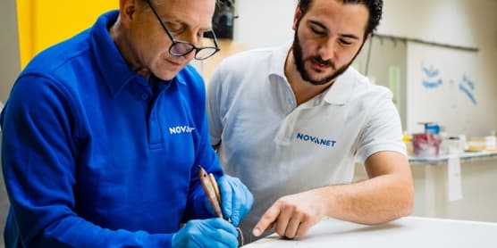 Twee mannen met shirt van Novanet staan gebogen over een tafel met een schilderkwast in de hand