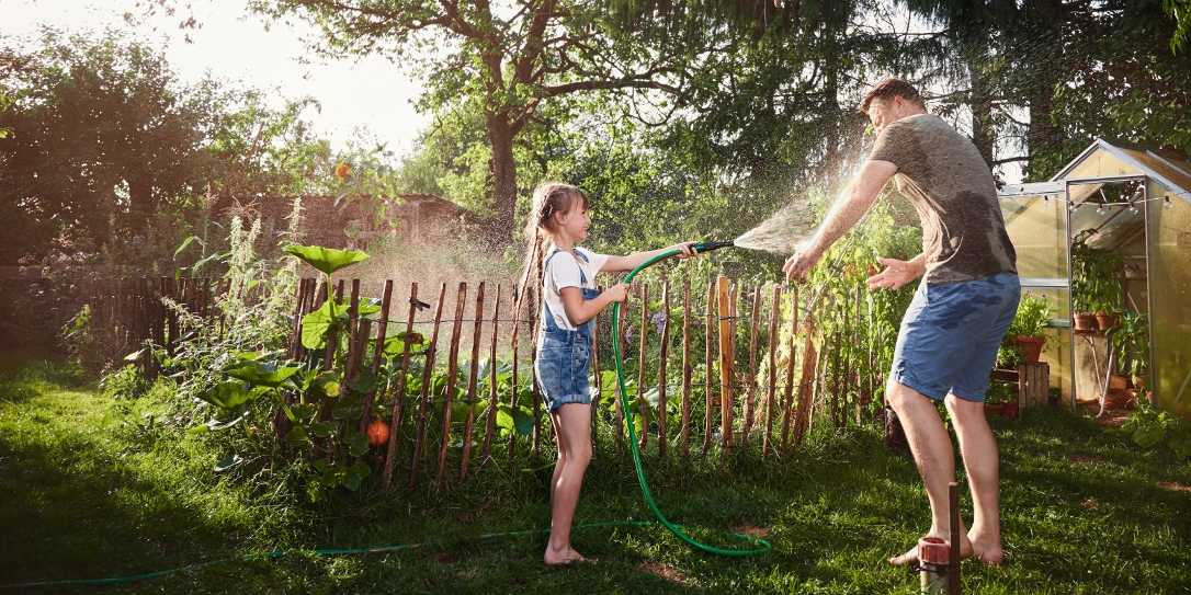 Vader en dochter hebben waterpret met een sproeier in de tuin