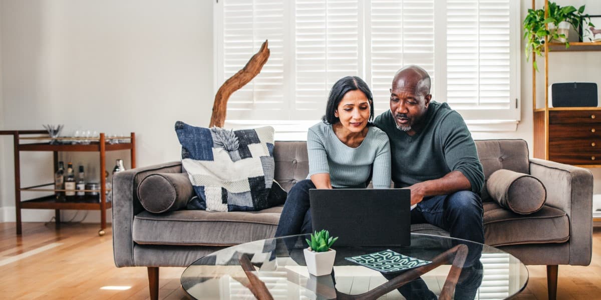 Man en vrouw zitten op de bank kijkend naar een laptop.