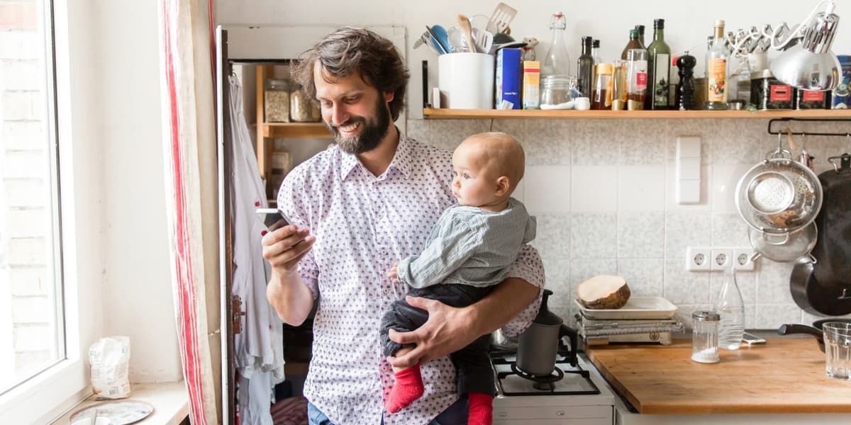 man met baby op de arm checkt telefoon