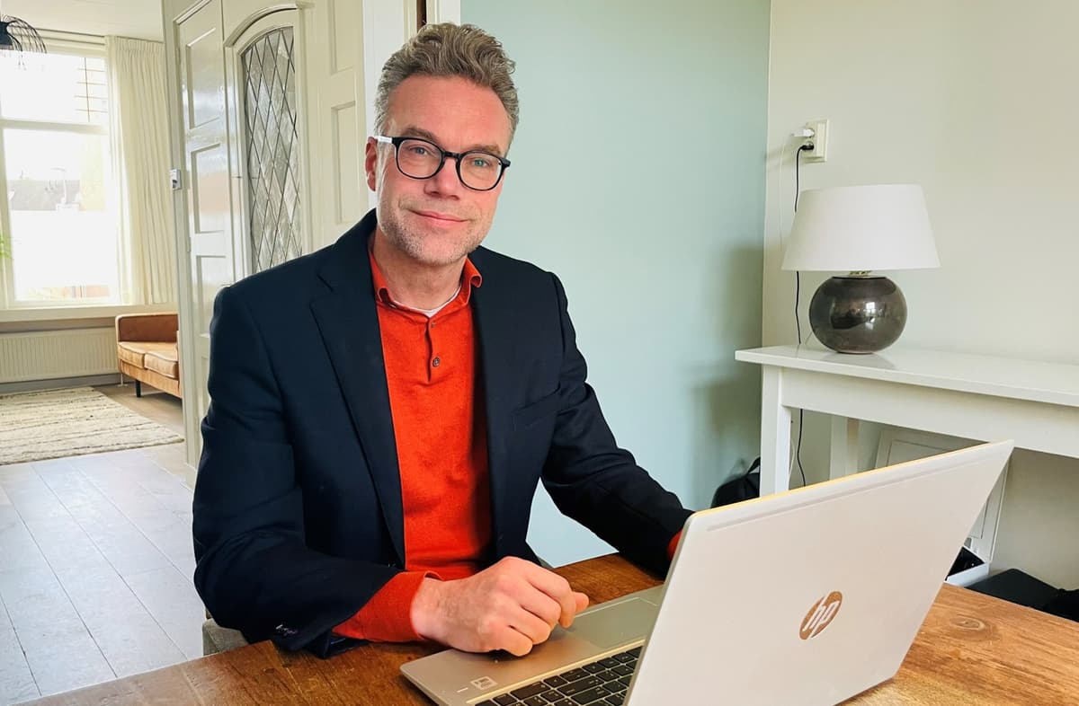 Niels Nijland zit aan tafel achter zijn laptop en kijkt de camera in