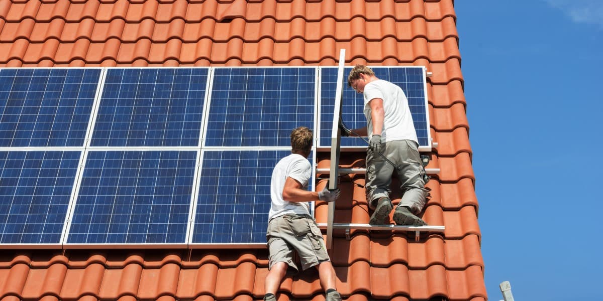 Twee mannen installeren zonnepanelen op het dak van een koopwoning