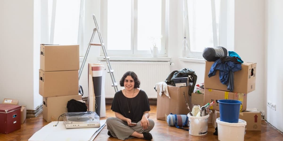 Jonge vrouw zit op de grond van haar nieuwe huis, tussen de verhuisdozen en klusspullen