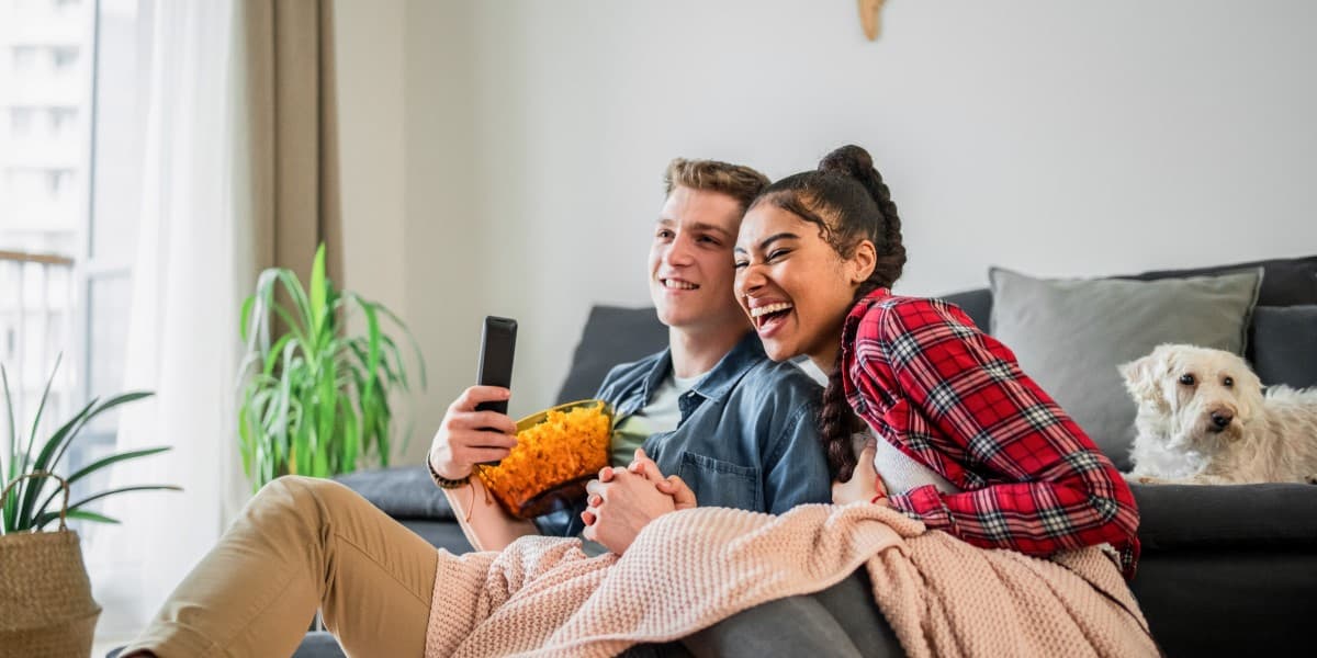 Studenten lachend met chips op de bank, ze kijken een film.