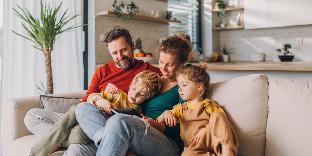 Vader, moeder en twee kinderen op de bank, gebruiken tablet