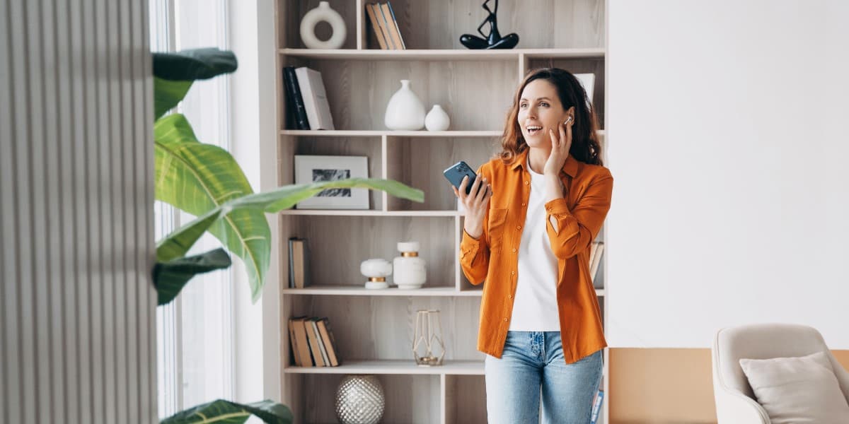 Vrouw belt met AirPods en haar iPhone terwijl ze loopt door haar woning