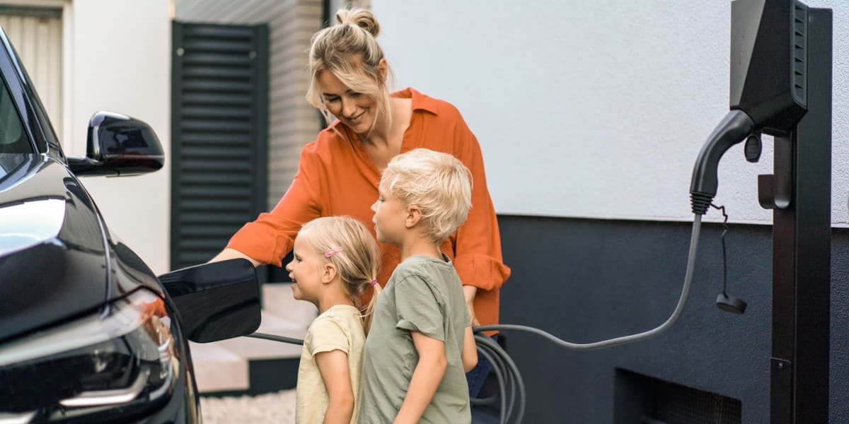 Moeder met kinderen laadt elektrische auto op aan de laadpaal voor hun huis
