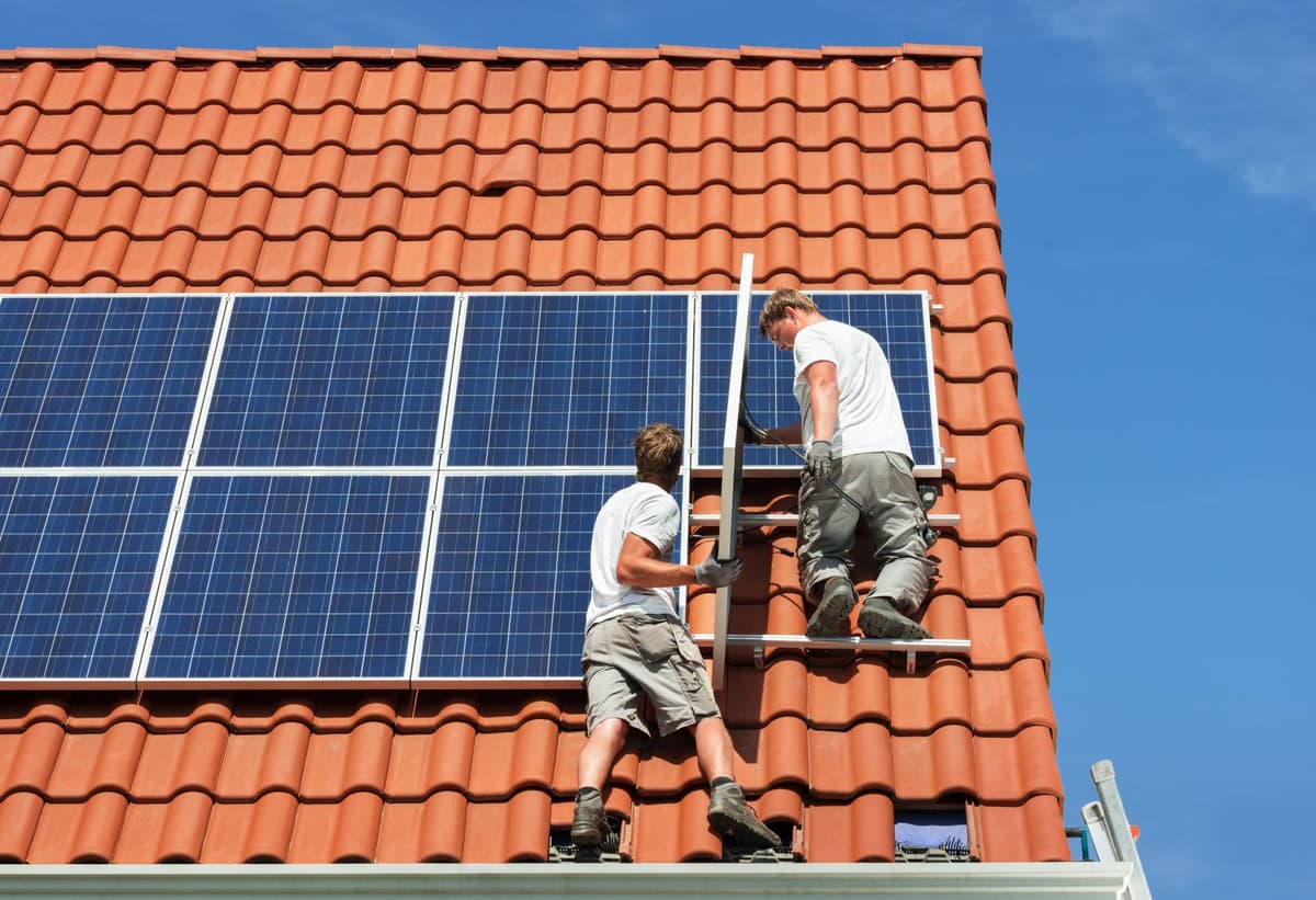 Twee mannen zijn zonnepanelen aan het installeren op het dak van een huis