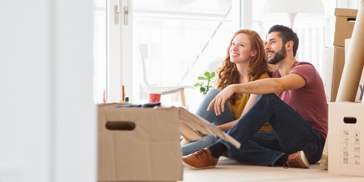 Stel zit op de vloer in hun nieuwe huis tussen de verhuisdozen