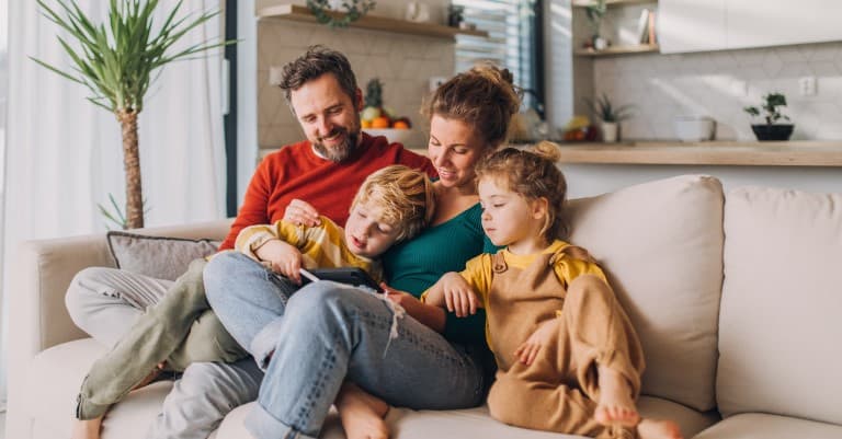Gezin met twee kinderen zit op de bank in de woonkamer en ze kijken op een tablet