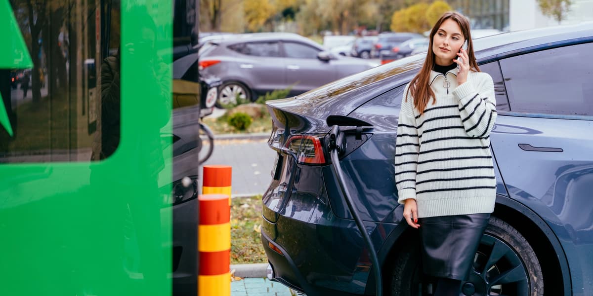 Jonge vrouw die voor haar Tesla staat te bellen en aan haar auto aan het opladen is.
