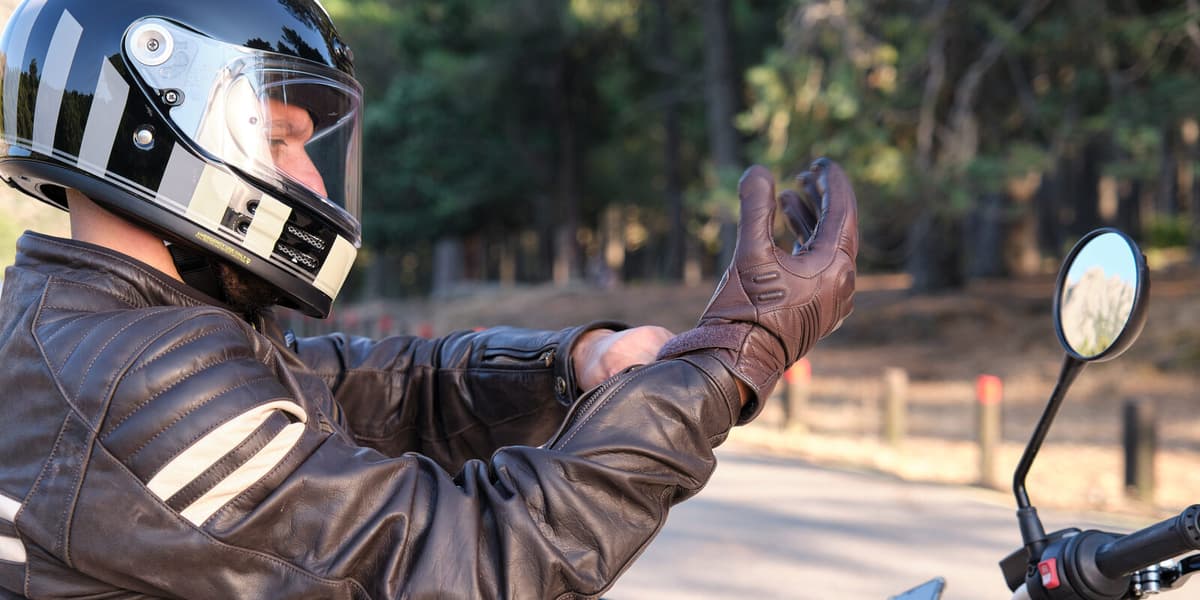 Hier zie je een afbeelding van een motorrijder met helm die zijn motorhandschoenen aantrekt