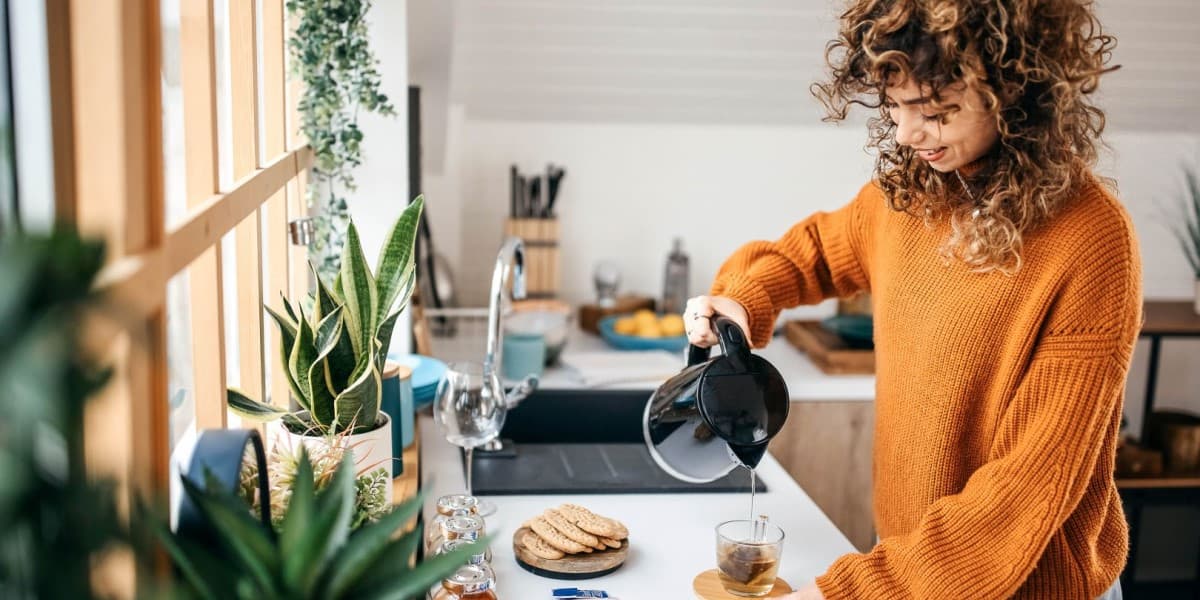 Vrouw staat bij het aanrecht in de keuken en schenkt thee in