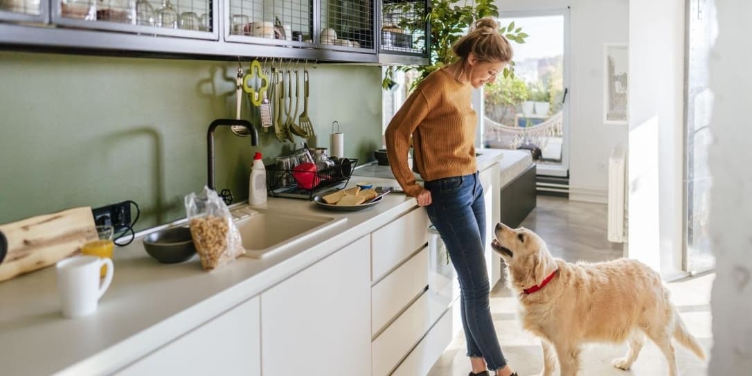 Vrouw leunt tegen aanrecht in de keuken en kijkt naar haar hond die voor haar staat