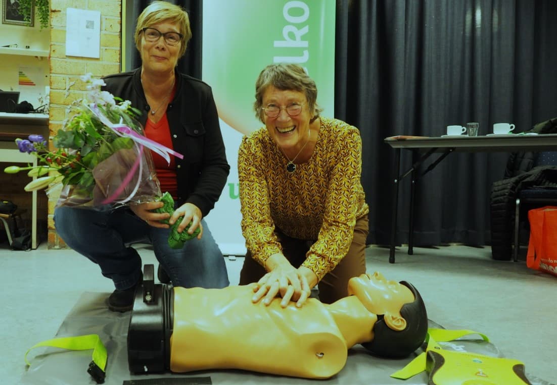 Aurinda Nieuwland heeft bloemen in haar hand naast een vrouw die haar AED training volgt en bezig met hartmassage.