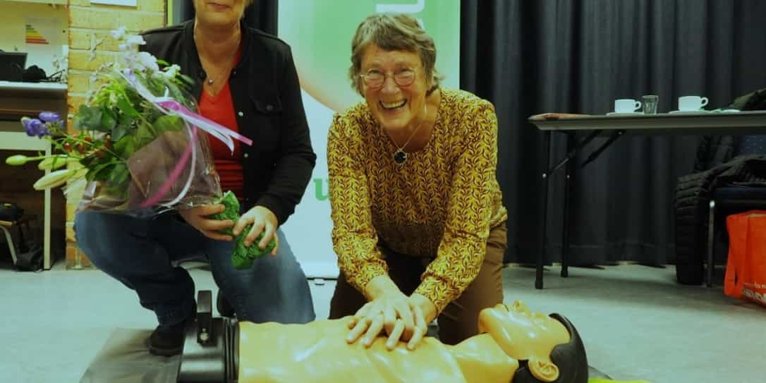 Aurinda Nieuwland heeft bloemen in haar hand naast een vrouw die haar AED training volgt en bezig met hartmassage.
