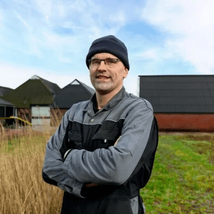 Boer Casper zelfverzekerd voor zijn boerderij, gekleed met muts en overall
