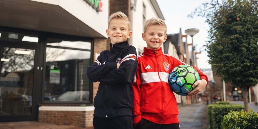 Twee jongens staan met een voetbal in de hand voor de Univé winkel in Oldenzaal