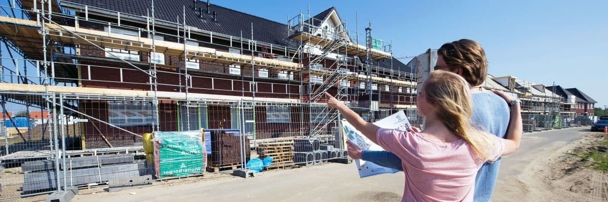 Stel staat voor een nieuwbouwwoning die in de steigers staat en wijst ernaar