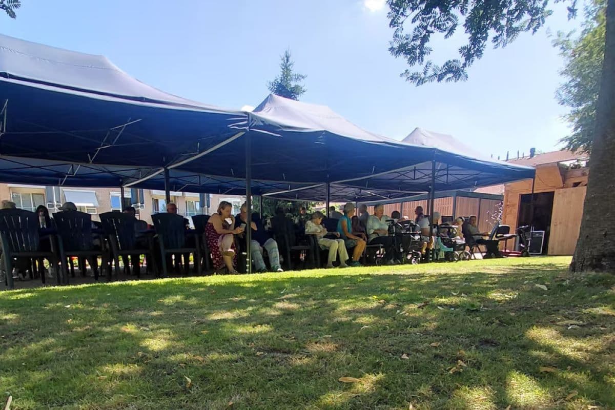 Buurtbewoners zitten gezamenlijk onder een opvouwbare partytent bij 't Hofke