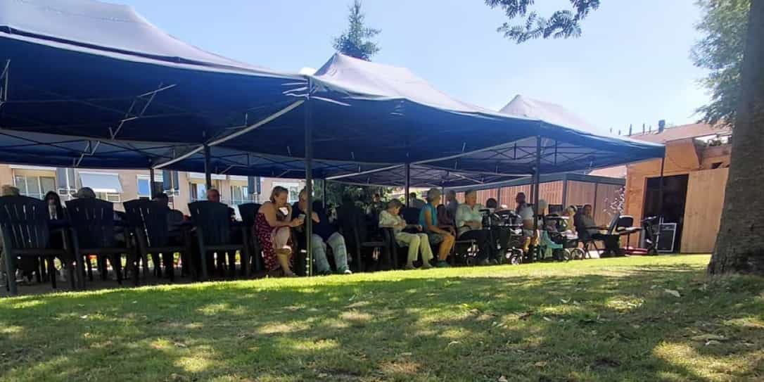 Buurtbewoners zitten gezamenlijk onder een opvouwbare partytent bij 't Hofke