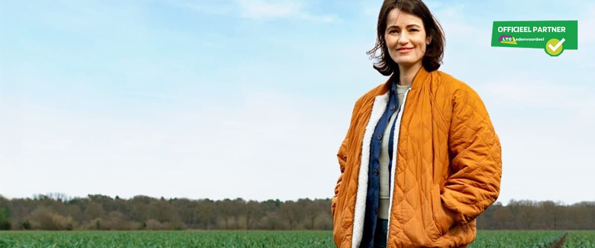 Vrouw in oranje jas staat in een landelijke omgeving met op de achtergrond een akker en bomen. Rechtsboven staat het label “Officieel partner LTO Ledenvoordeel”.