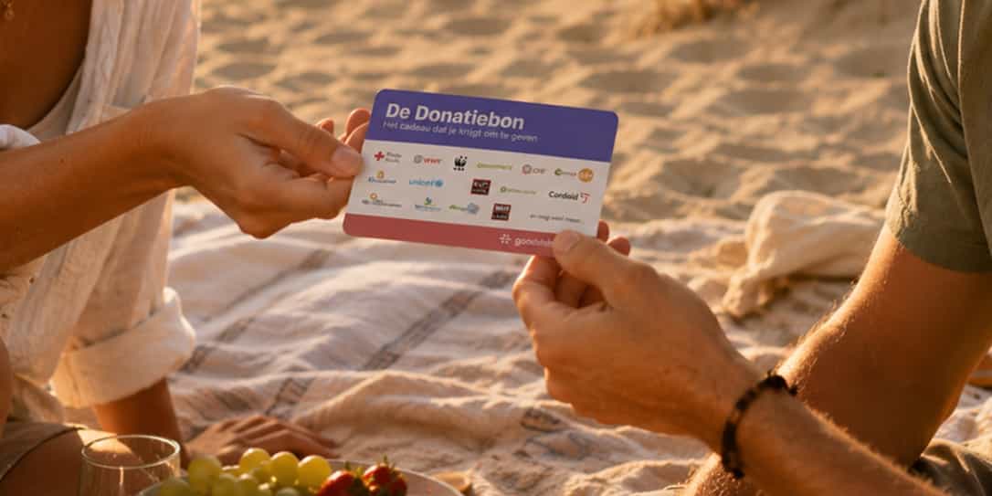 Een persoon geeft op het strand tijdens een picknick een cadeaukaart met de tekst “De Donatiebon – Het cadeau dat je krijgt om te geven” aan iemand anders.
