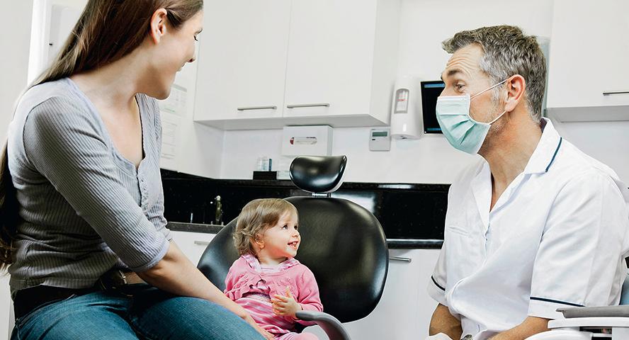 Kindje lachend naast haar moeder in de tandartsstoel