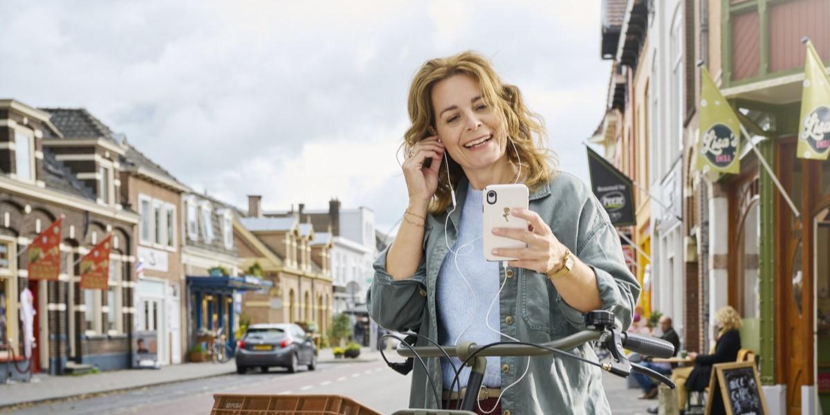 Vrouw staat naast haar fiets op straat en belt met haar mobiele telefoon